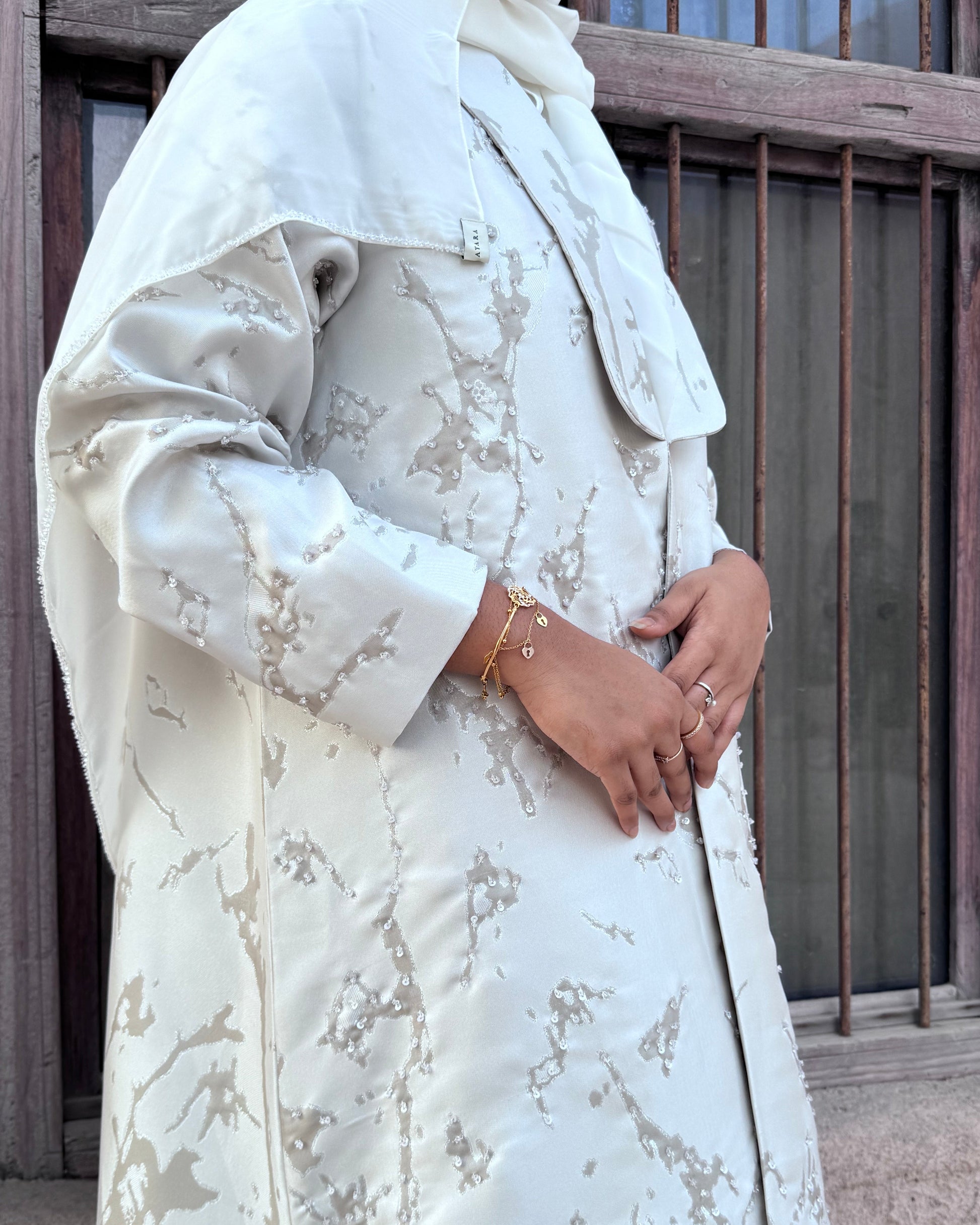 Close-up of a person wearing a white lace dress with floral patterns, standing against a wooden background.